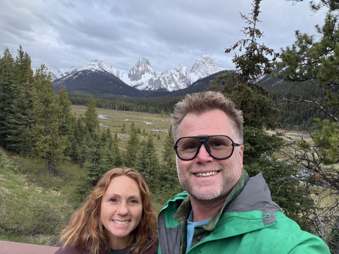 Joe and a companion at an overlook with snowcapped peaks near Banff